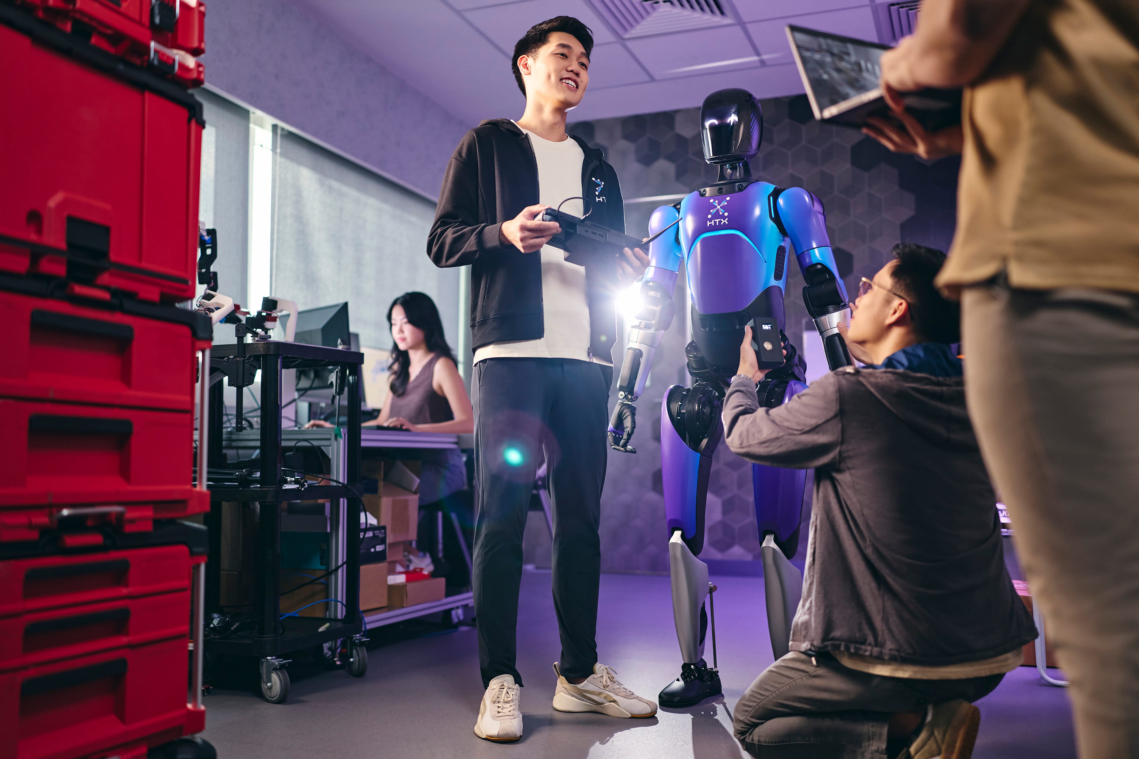 Engineers working on a blue/purple HTX robot with a remote control and laptop in a lab.